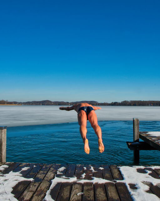 Ice swimming at Wörthsee One of the winter swimmers jumps from the snow-covered footbridge into the Wörthsee