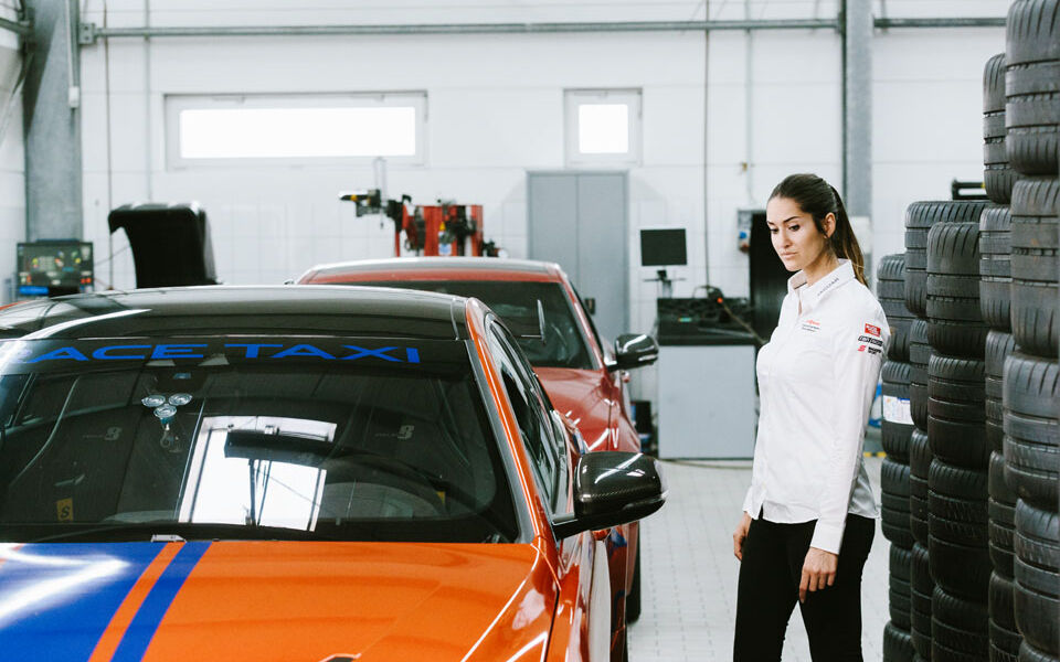 Interview with racing driver Célia Martin Racing driver Célia Martin stands next to an orange and blue Jaguar racing car in a garage