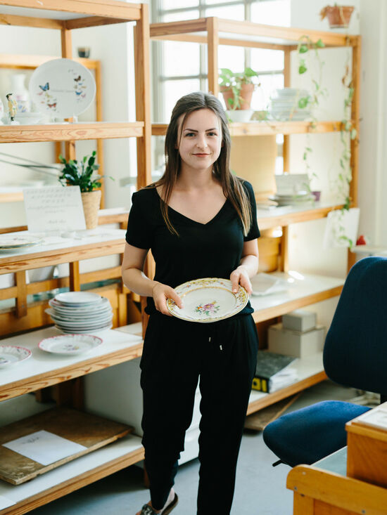 Michelle Sosna standing in front of a shelf, holding a painted porcelain plate