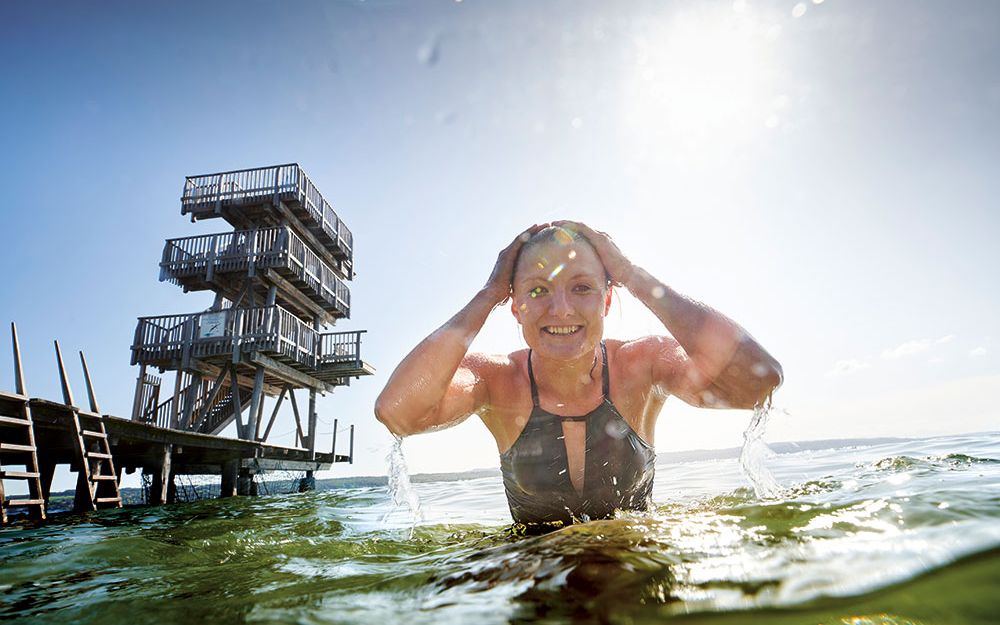 Interview Iris Schmidbauer Iris Schmidbauer emerges from the Ammersee. In the background the diving platform of the lido Utting