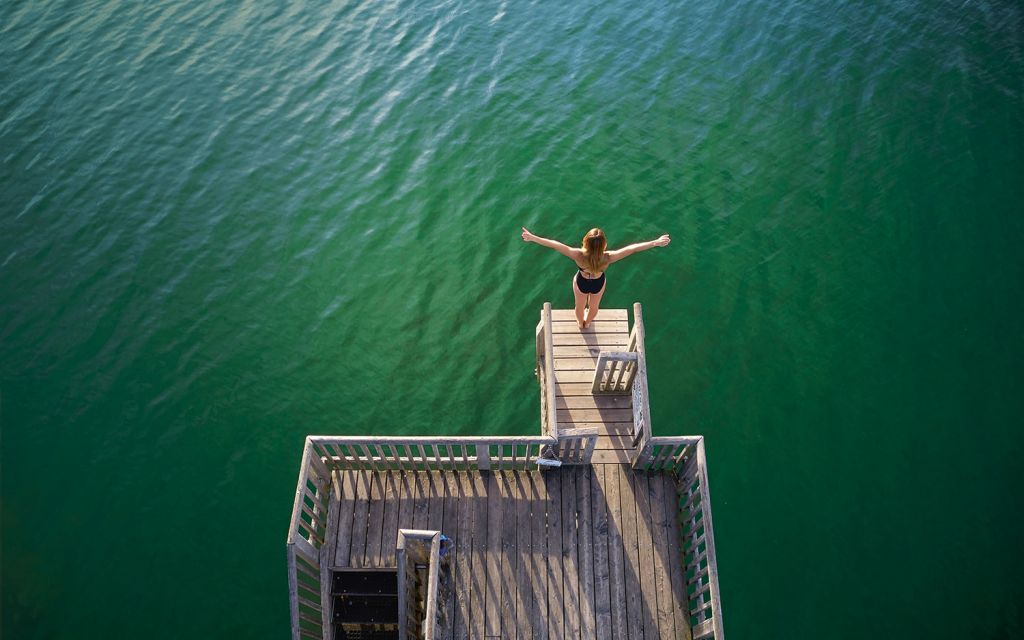 Interview Iris Schmidbauer at "Strandbad Utting" Iris Schmidbauer stands on a springboard with outstretched arms above the Ammersee in Utting