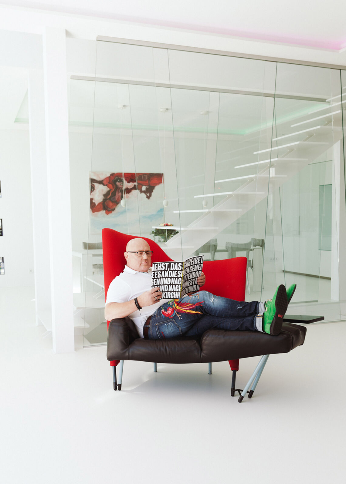 BORA Magazine: Behind-the-scenes at the homestory in Siegen Bald man sitting on red-black armchair reading a magazine
