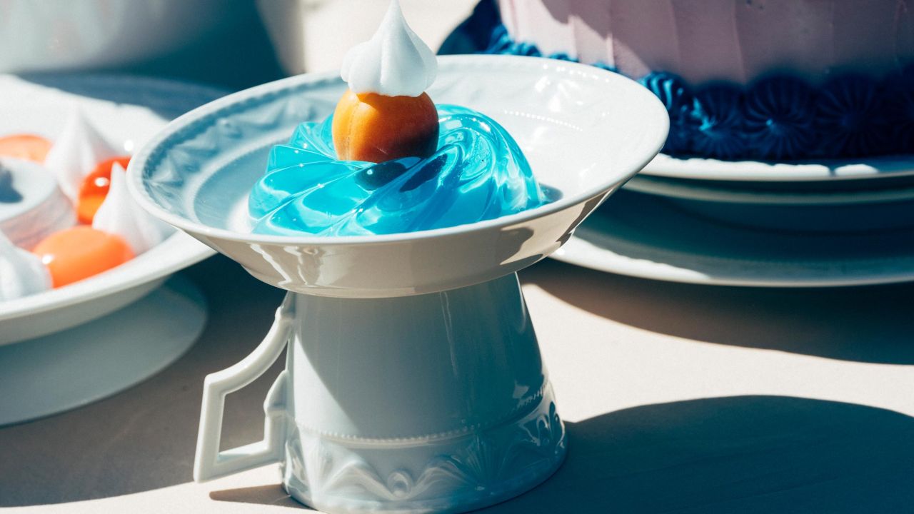 Nahaufnahme eines Tellers mit einem blauen Wackelpudding und einer Frucht, der auf einer umgedrehten Tasse steht.