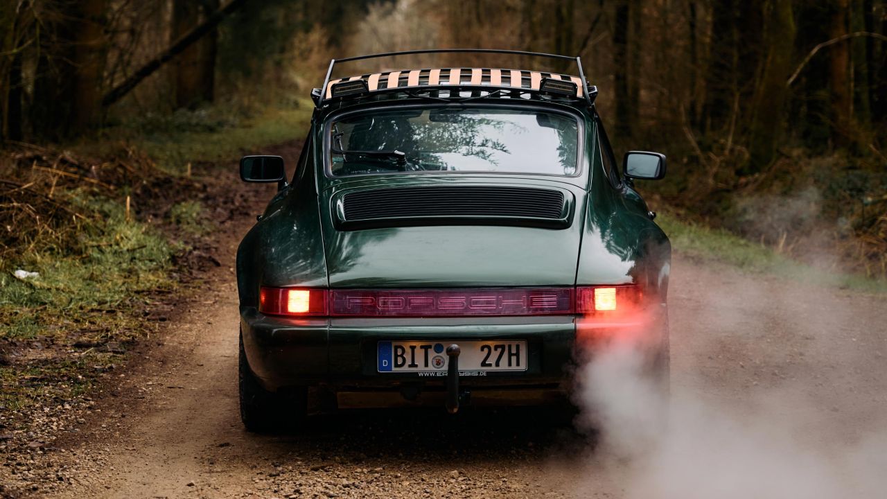 Rear view of a dark green Porsche 911 with roof rack driving on a forest road Rear view of a dark green Porsche 911 with roof rack driving on a forest road
