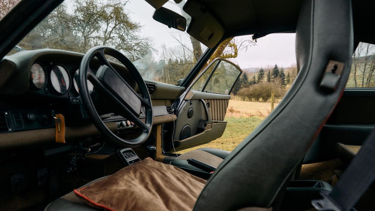 Interior view of a green Porsche 911 with black leather seats, beige seat cushions, and open door Interior view of a green Porsche 911 with black leather seats, beige seat cushions, and open door